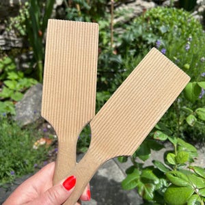 May include: Two light-colored wooden gnocchi boards with a rectangular paddle shape and a series of parallel, vertical ridges running along the entire length of the flat surface, each featuring a short, integrated handle for a secure grip.