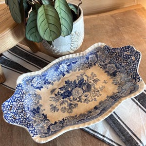 May include: An oblong ceramic serving dish featuring a blue and white floral pattern with intricate lattice detailing on the handles. The center displays a detailed bouquet of flowers, while the scalloped edges are finished with a decorative border.