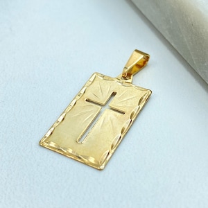 Puede incluir: Un colgante de oro en forma de rectángulo con una cruz recortada en el centro. La cruz tiene un diseño de rayos de sol.