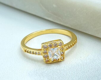 May include: A gold-toned ring featuring a central square-cut clear stone surrounded by a halo of smaller clear stones. The band is also adorned with a row of tiny clear stones along each side, creating a continuous sparkling effect.