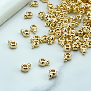 May include: A large pile of gold-colored metal bead caps with a small loop on top. There are also a few bead caps scattered around the pile.