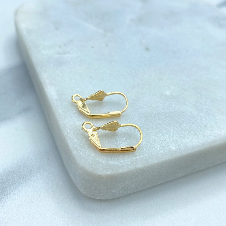 May include: Two gold-toned earring hooks with a spring-loaded closure. The hooks are on a white marble surface.
