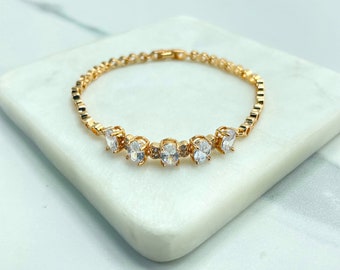 Puede incluir: Una pulsera de cadena en tono dorado con cinco piedras blancas transparentes de corte ovalado dispuestas en fila. La pulsera presenta un diseño de eslabones delicados y un mecanismo de cierre seguro con acabado metálico pulido.