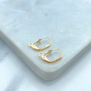 May include: Two gold-toned earring hooks, also known as ear wires, are shown on a white marble surface. The hooks are made of metal and have a simple, classic design.