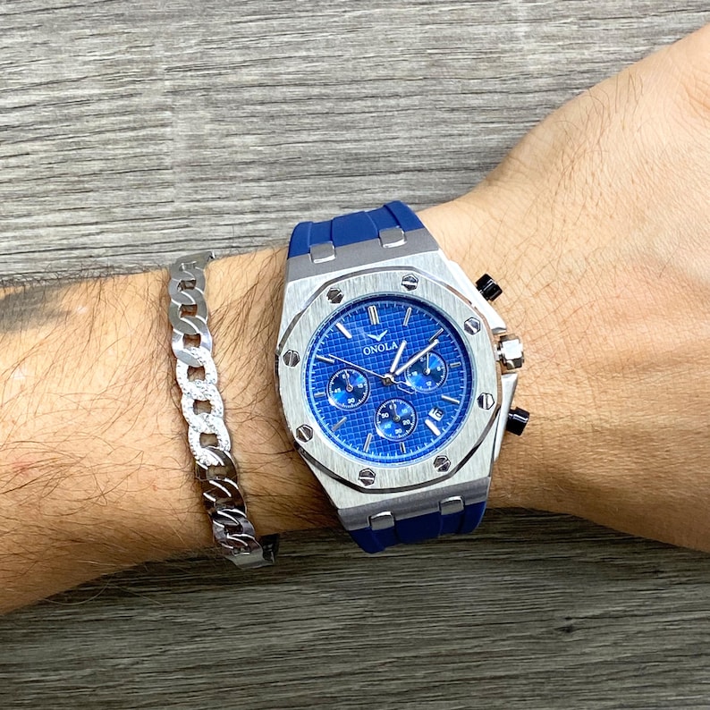 May include: A silver and blue chronograph wristwatch with a blue rubber band. The watch face has a blue background with white markings and the word "ONOLA" printed on it.