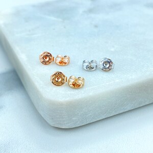 May include: Three pairs of earring backs in gold, rose gold, and silver. The backs are round with a small hole in the center.