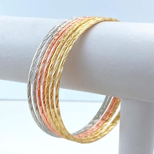 Può includere: Set di cinque braccialetti in oro, argento e oro rosa. I braccialetti sono sottili e hanno un design testurizzato e intrecciato.