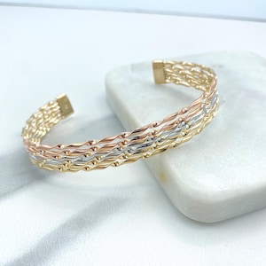 Puede incluir: Un brazalete de oro, plata y oro rosa con un diseño tejido. El brazalete está abierto y tiene una forma curva.