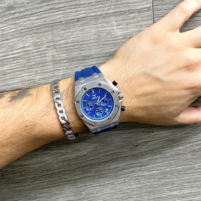 May include: A silver and blue chronograph wristwatch with a blue rubber band. The watch face has silver hands and markers, and the brand name "ONOLA" is printed on the face.