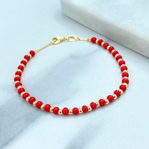 May include: A gold chain bracelet with red beads. The bracelet is made of small, round beads that are evenly spaced.