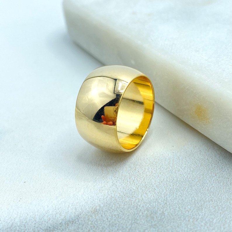May include: A polished gold ring with a rounded, domed design. The ring reflects the surrounding environment, showcasing a smooth, shiny surface. The ring is a simple, elegant piece of jewelry.