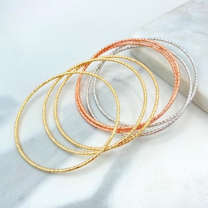 May include: Set of five gold, silver, and rose gold bangle bracelets. The bracelets are thin and have a textured surface.