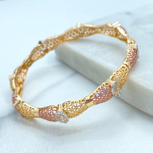May include: A gold-toned bracelet with a unique, openwork design. The bracelet features sections of gold, rose gold, and silver-toned metal. The openwork pattern creates a delicate, yet eye-catching aesthetic. The bracelet is a piece of jewelry.