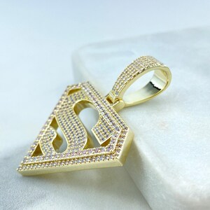 Puede incluir: Colgante de tono dorado con un dise&ntilde;o de logotipo de Superman con piedras de circonita c&uacute;bica transparentes.