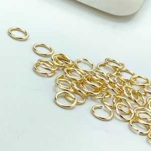 Könnte beinhalten: Ein Haufen goldener Sprungringe, eine Art Schmuckzubehör, auf einer weißen Oberfläche. Die Ringe sind klein und filigran und perfekt zum Schmuckmachen.