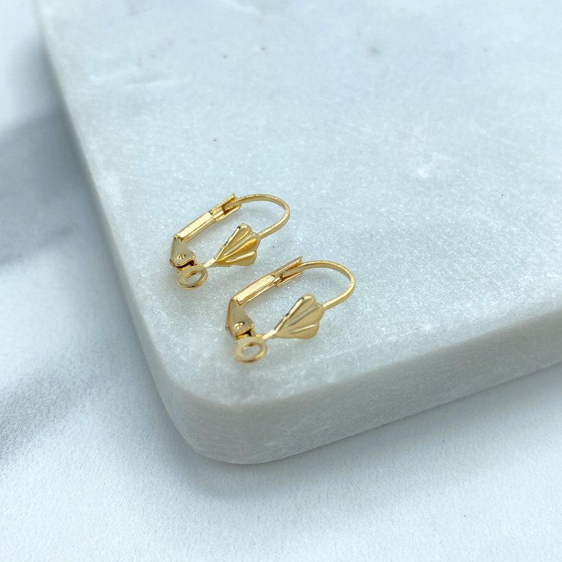 May include: Two gold-toned earring findings with a fan-shaped design. The findings are on a white marble surface.