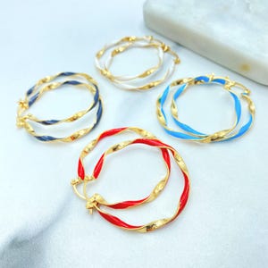 May include: Gold-tone hoop earrings with a twisted design, featuring red, blue, white, and navy enamel accents. The earrings are displayed on a white surface, showcasing their vibrant colors and intricate details.
