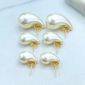 May include: Six pairs of teardrop-shaped pearl earrings with gold-colored posts. The earrings have a creamy white color and a smooth, glossy finish. The earrings are arranged in two rows of three.