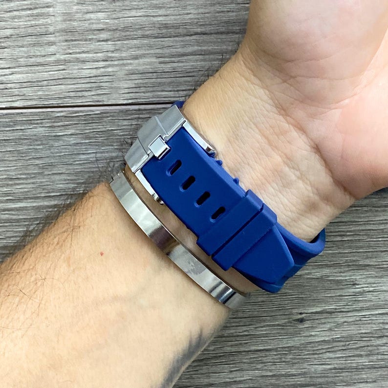 May include: A blue silicone watch band with a silver buckle. The band is on a person's wrist.