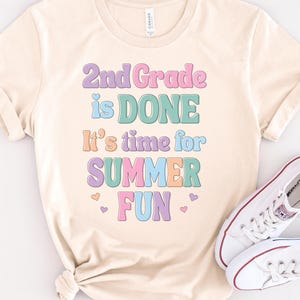May include: A light beige t-shirt with the text "2nd Grade is DONE It's time for SUMMER FUN" in colorful letters with hearts.