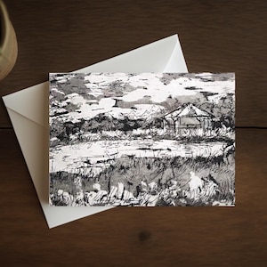 Könnte beinhalten: Ein schwarz-weiß Landschaftskunst-Druck mit einem kleinen Gebäude auf einem Feld unter einem bewölkten Himmel. Das Kunstwerk befindet sich auf einer weißen Karte, die auf einem weißen Umschlag liegt. Die Szene ist im Skizzenstil gehalten.