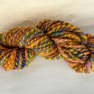 May include: A skein of yarn in a mix of yellow, orange, blue, and purple colors. The yarn is hand-spun and has a fuzzy texture.
