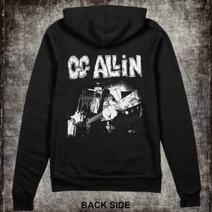May include: Black hooded sweatshirt with a white graphic print of musician GG Allin playing a guitar.