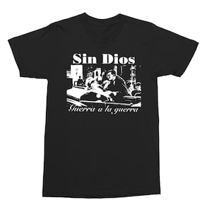 May include: Black t-shirt with a white graphic print of a scene from a movie. The text "Sin Dios" and "Guerra a la guerra" is printed on the shirt.