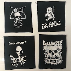 May include: Four black and white iron-on patches. The top left patch features a skull with a gas mask and the text "DOOM DOOMED AGAIN". The top right patch features a woman with long hair and the text "DR. KNOW". The bottom left patch features a man with a skull face and the text "DISCHARGE PROTECT AND SURVIVE". The bottom right patch features three skulls with the text "DISCHARGE UK-HARDCORE".