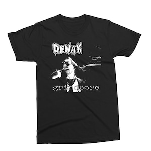 May include: Black t-shirt with a white graphic of a person singing into a microphone. The text "DENAK grindcore" is printed below the image.