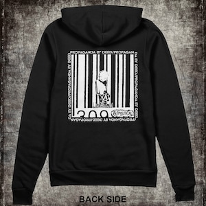 May include: Black hooded sweatshirt with a white graphic print of a barcode with a stick figure holding an anarchy symbol inside. The text "PROPAGANDA BY DEED/PROPAGANDA BY DEED" is printed on either side of the barcode. The text "A/POLITICAL" is printed below the barcode. The text "200" is printed above the barcode.