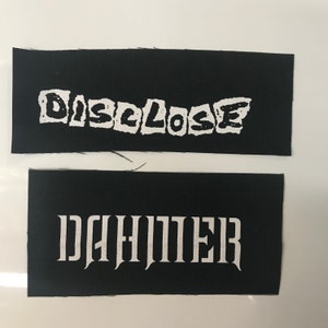 May include: Two black fabric patches with white text. The top patch says "DISCLOSE" in a jagged font. The bottom patch says "DAHMER" in a gothic font.