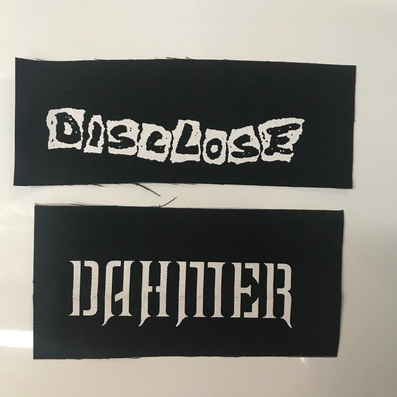 May include: Two black fabric patches with white text. The top patch says "DISCLOSE" in a jagged font. The bottom patch says "DAHMER" in a gothic font.