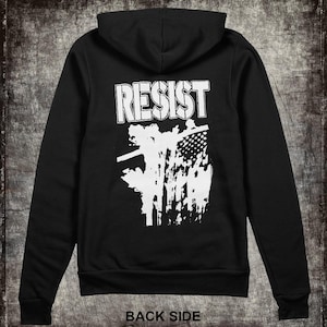 May include: Black hooded sweatshirt with a white graphic print that says "RESIST" and a stylized image of a fence with barbed wire. The back of the sweatshirt has the words "BACK SIDE" printed below the graphic.