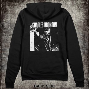 May include: Black zippered hoodie with a white graphic print of Charles Bronson holding a gun. The graphic is on the back of the hoodie.