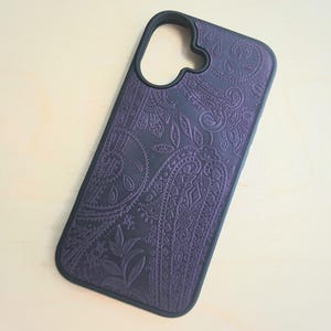 May include: A dark purple smartphone case featuring an embossed paisley pattern across the back surface. The case has a black border and a large, irregular cutout at the top for a camera module, maintaining a slim and protective rectangular shape.