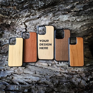 May include: Five rectangular phone cases with black frames and wooden back panels in varying shades of light to dark brown. The center case features the black text YOUR DESIGN HERE. Each case has a square cutout for a camera lens.