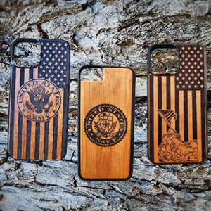 May include: Three rectangular phone cases with rounded corners and camera cutouts. The left case features a laser-engraved American flag and the United States Army seal. The centre case shows the United States Navy seal. The right case displays an American flag and the Iwo Jima memorial scene.
