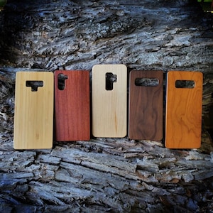 May include: Five rectangular phone cases made of different wood grains and tones, arranged in a row. Each case features a specific cutout for a camera lens and flash, showcasing light bamboo, reddish-brown, pale maple, dark walnut, and amber cherry wood.