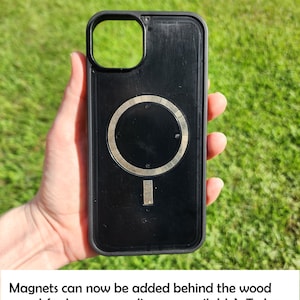 A hand holding a black phone case with a silver circular magnet on it, set against a grassy background.