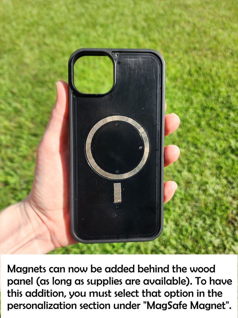 A hand holding a black phone case with a silver circular magnet on it, set against a grassy background.
