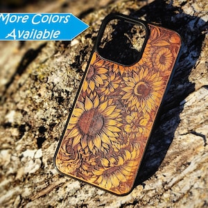 May include: A rectangular phone case with a black border and a wood-toned back panel featuring an intricate laser-engraved sunflower pattern. The text "More Colors Available" appears in a blue banner at the top left of the image.