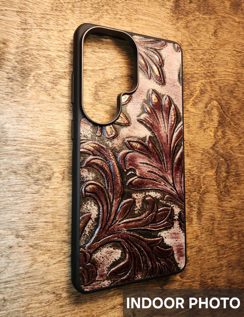 May include: A black phone case with a detailed, embossed floral design in shades of brown and burgundy. The case has a textured appearance and the words "INDOOR PHOTO" are visible at the bottom.