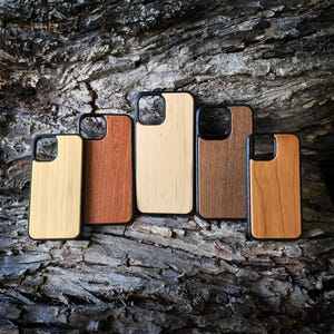 May include: Five rectangular phone cases with black frames and distinct wood grain back panels in varying shades of light, medium, and dark brown. Each case features a square camera cutout in the upper left corner and a smooth, flat surface.