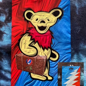 May include: A rectangular luggage tag featuring a yellow bear with a red scarf and a brown suitcase. The background is split diagonally, with red and blue sections. A smaller tag with a lightning bolt design is also visible.
