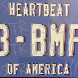 May include: A blue metal license plate with white text that reads "HEARTBEAT - 33-BMFS OF AMERICA".