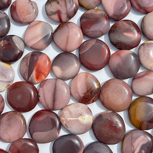 May include: A selection of polished stones in burgundy, mauve, and cream hues. The stones are smooth, rounded, and display diverse patterns of colour and veining. The close-up arrangement highlights the natural beauty of the stones.