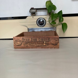 May include: A wooden box with the text "Your Name Bakery" and the words "Baked & Served in Your Location" on it. The box is brown and has a rustic look.