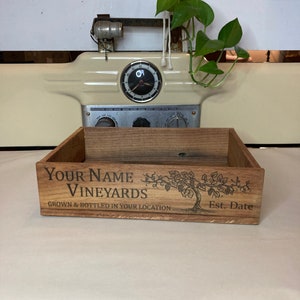 May include: A wooden box with the text "YOUR NAME VINEYARDS" and "GROWN & BOTTLED IN YOUR LOCATION" printed on the front. The box also has a vine and grapes design and the text "Est. Date" on the front.