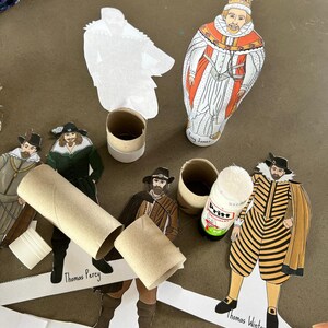 Op de afbeelding: Papieren uitsparingen van historische figuren, waaronder koning James, Thomas Percy, Guy Fawkes en Thomas Wintour, zijn gerangschikt met kartonnen buizen en lijm. De figuren zijn gekleed in historische kleding, met gedetailleerde illustraties en tekstlabels.
